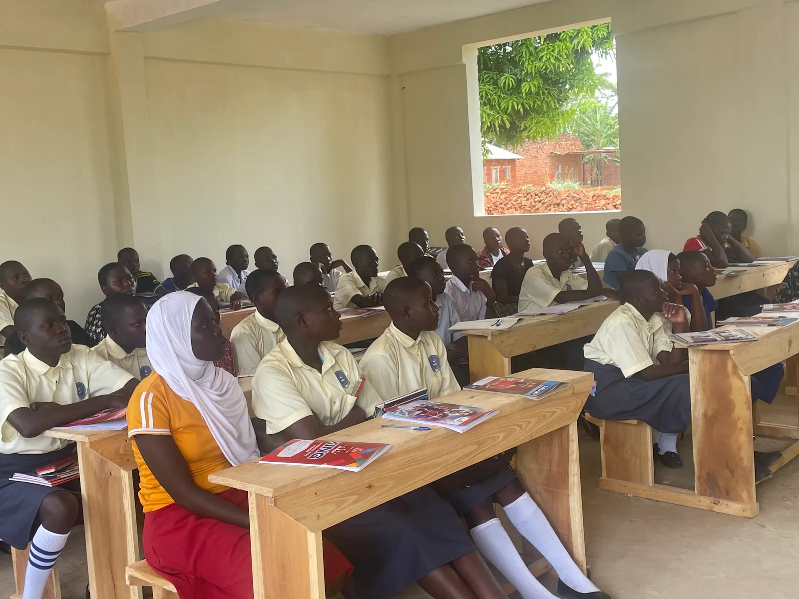 Students in uniform seated at wooden desks listening in a bright classroom