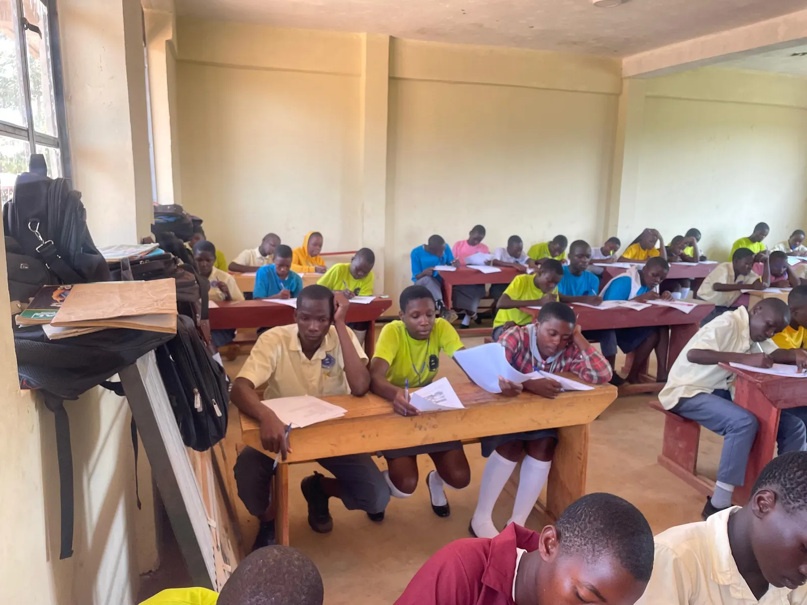 Students in uniform write at wooden desks during a lesson