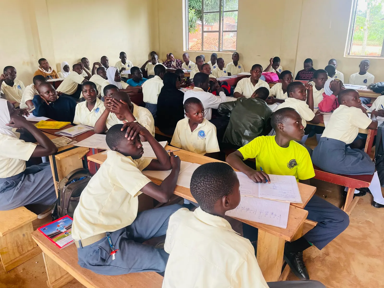 Students in yellow and white uniforms sit at wooden desks through a long examination hall