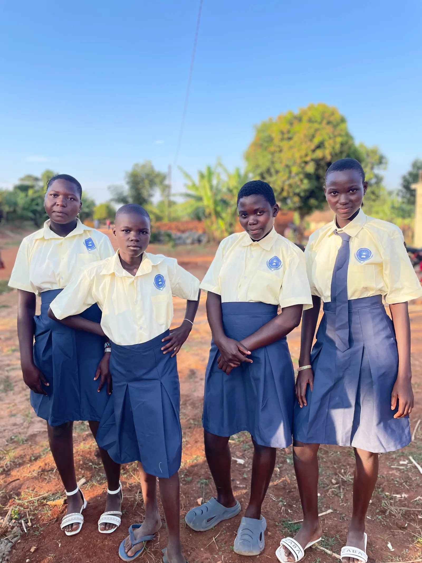 Four students in yellow shirts and navy skirts standing together on the school grounds
