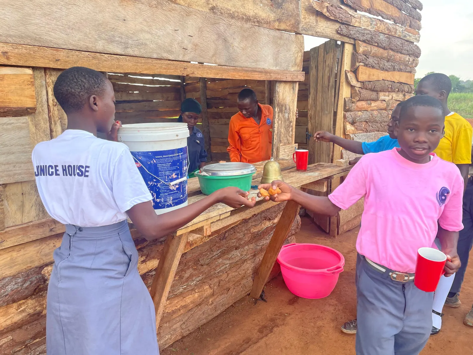 A staff member serves food through the kitchen window while students wait with plates