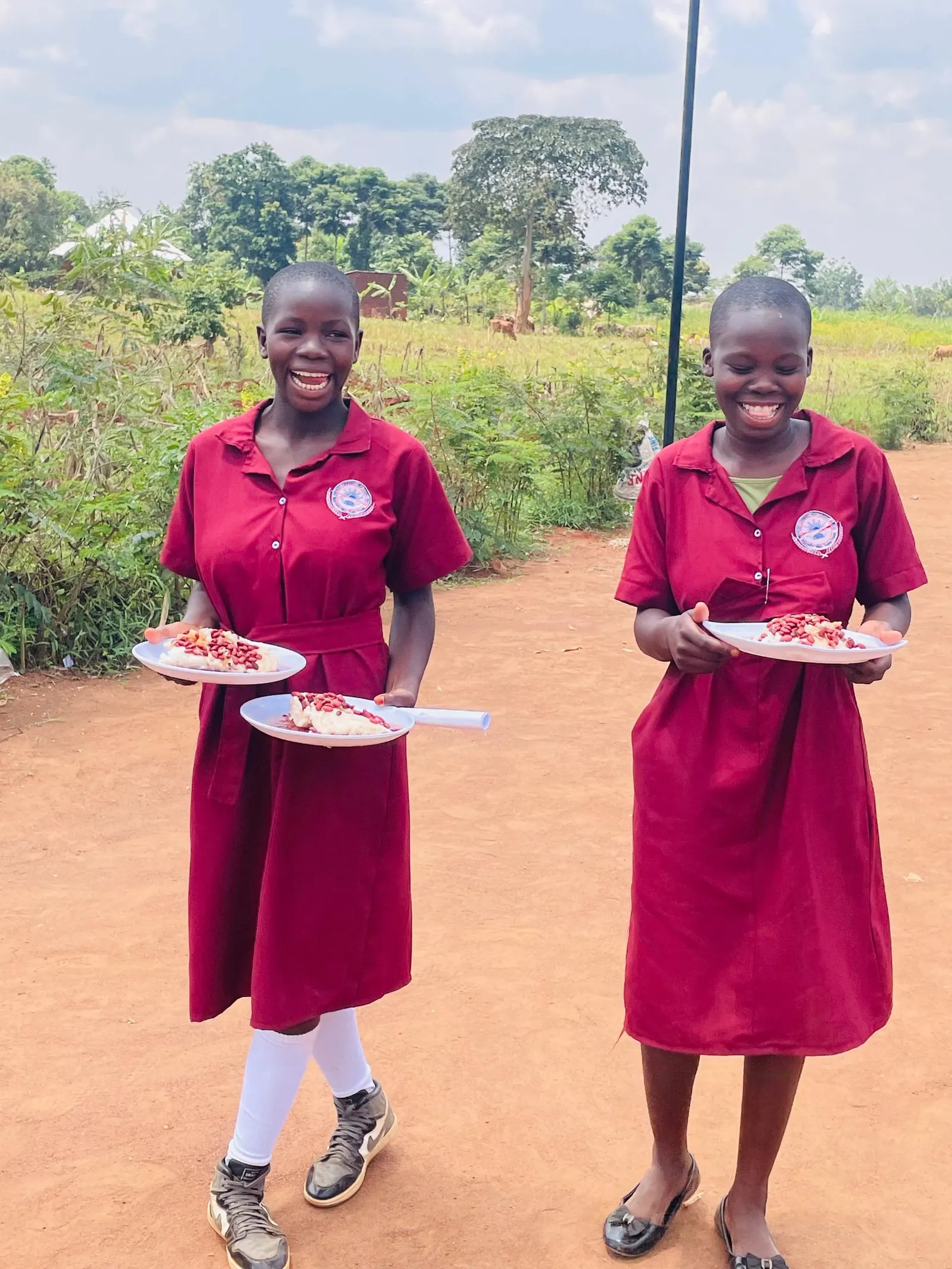 Two students hold plates of beans and maize meal at lunch