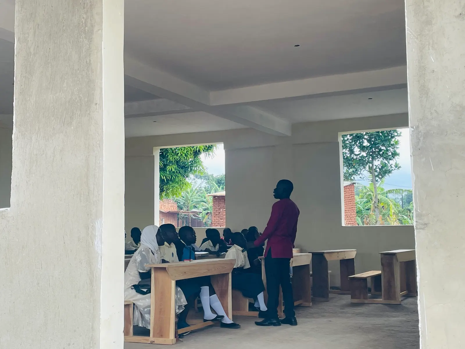 A teacher stands before students at desks in an open-sided classroom